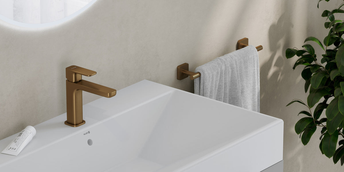 Basin mixer in brushed bronze on a white washbasin, with a towel rail and a plant