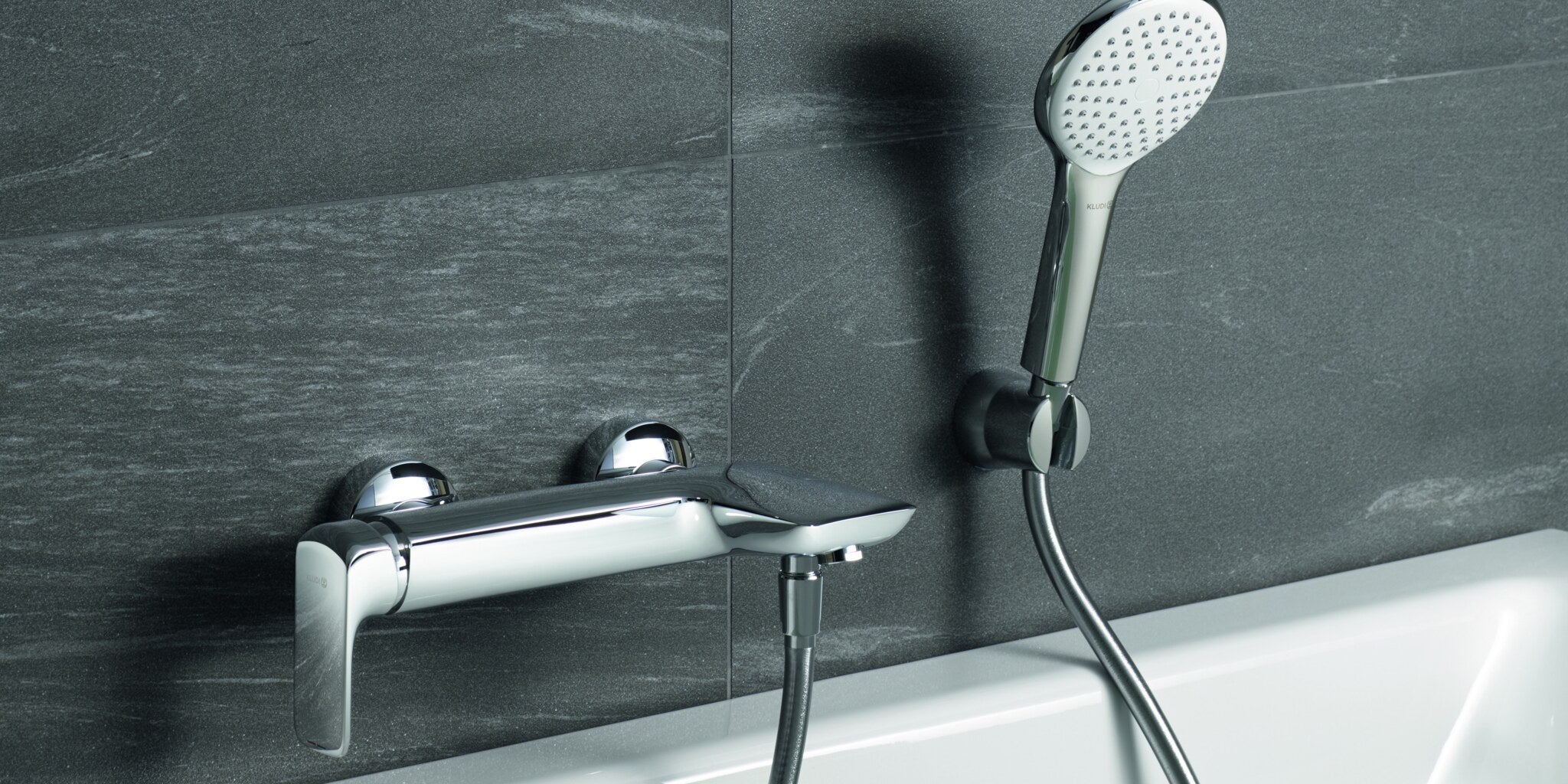 Bath mixer with a hand shower in its wall holder on a slate wall