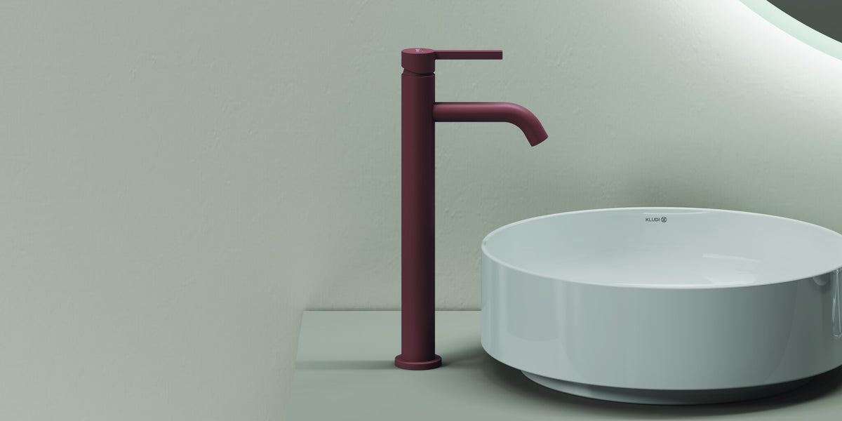 Round countertop basin with a tall basin mixer under a backlit mirror