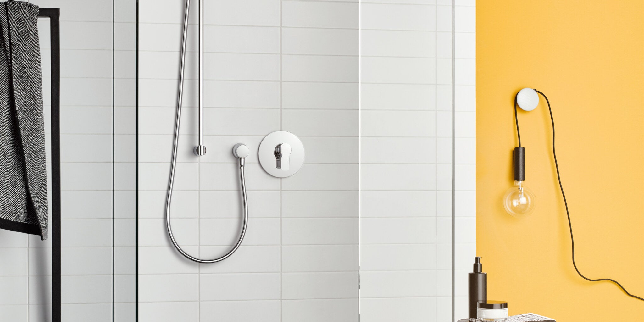 Walk-in shower with a concealed single lever mixer, beside a yellow wall with a bare bulb