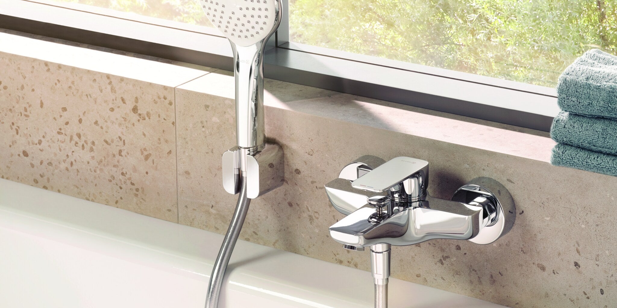 Wall-mounted bath mixer with hand shower on a concrete wall beside a window