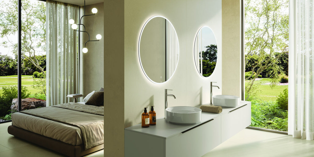 Double vanity with two countertop basins and oval backlit mirrors by a garden window