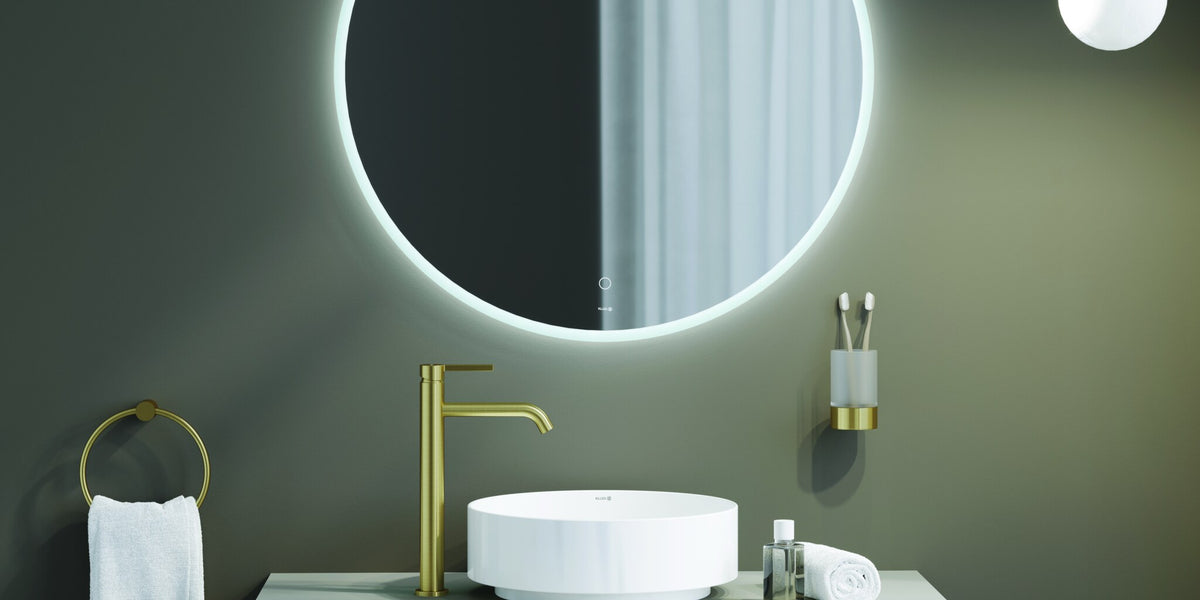 Wall shelf, towel ring and tumbler holder in brushed gold around a lit mirror