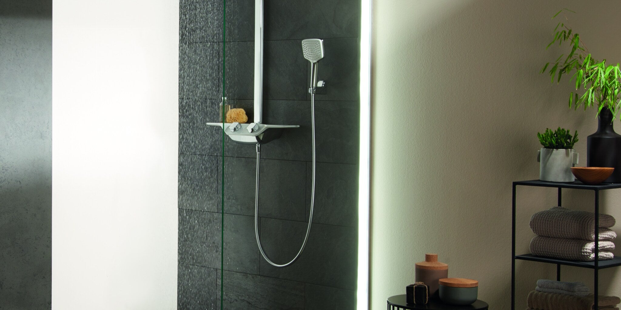 Shower column with a hand shower and a shelf on a dark tiled wall