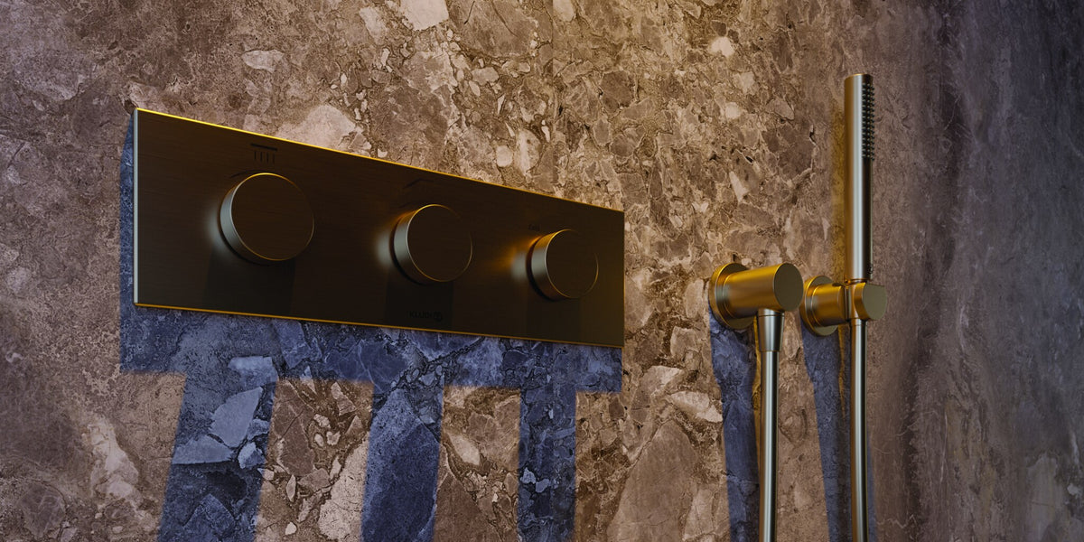 Concealed thermostat plate in brushed bronze on a marble shower wall