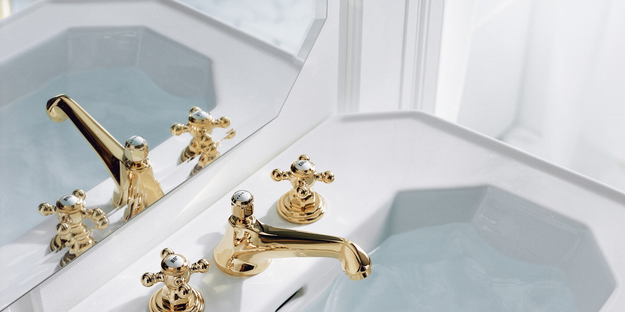 Classic three-hole set with cross handles in gold on a bath surround